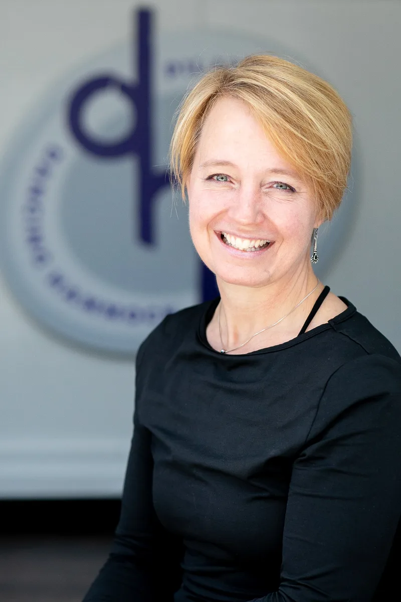 Silja Meier Burns, founder of Dancing Hammock Pilates, laughing in front of the DHP logo